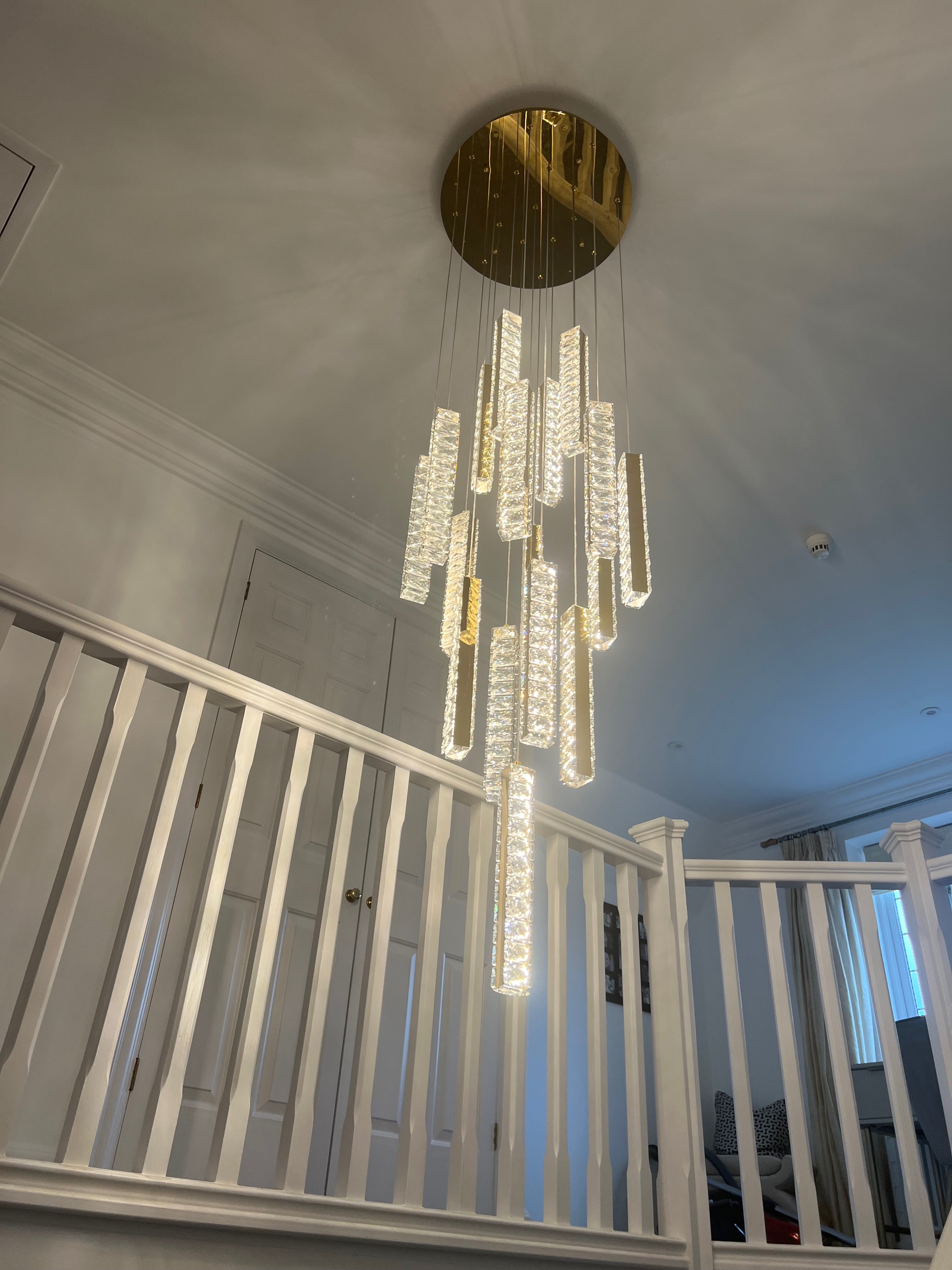 Luxury crystal pendant staircase chandelier cascading through a modern stairwell creating an elegant statement lighting feature
