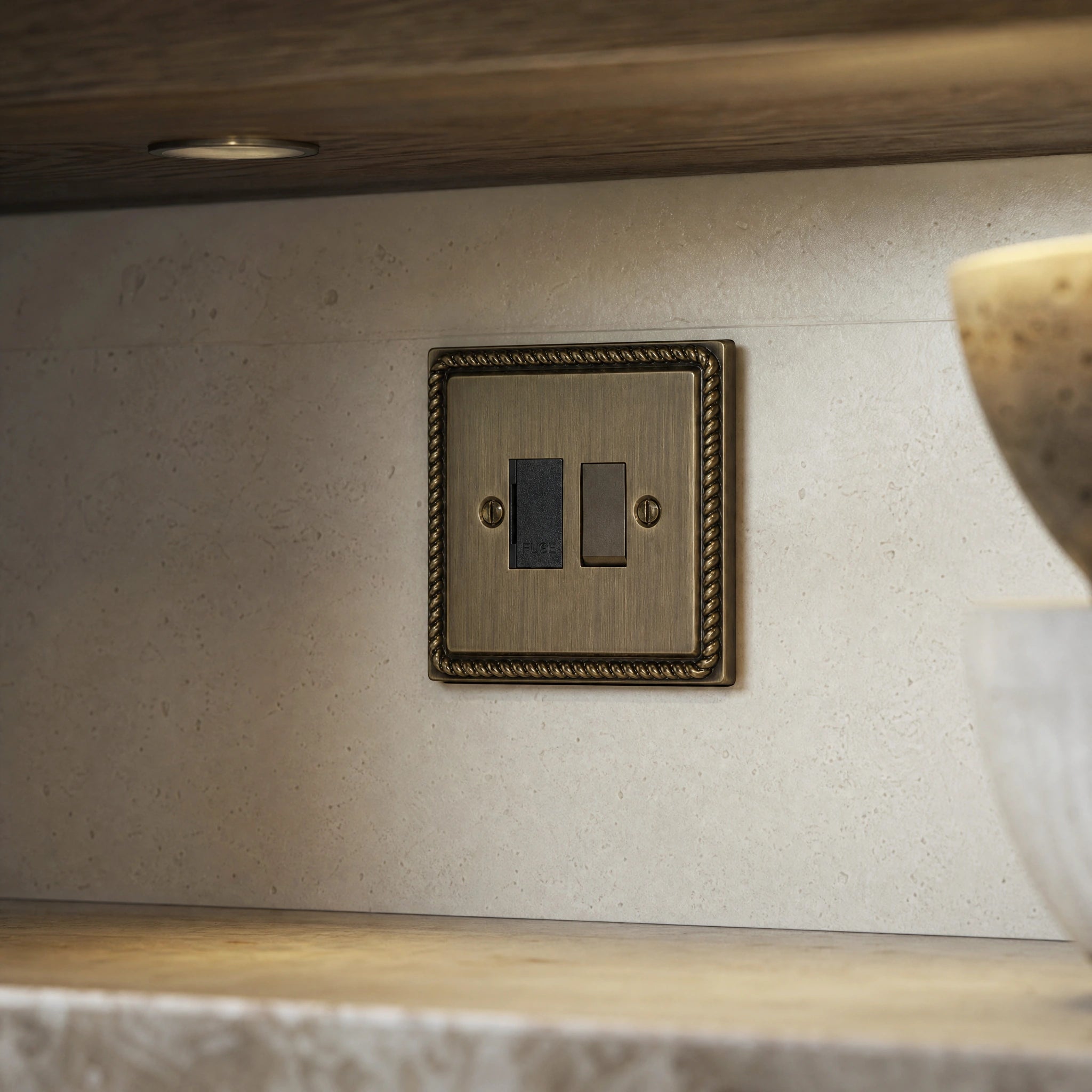 Close-up of a luxury antique brass fused spur installed within discreet below-cabinet utility or kitchen appliance zone in a high-end residence by VORELLI®.