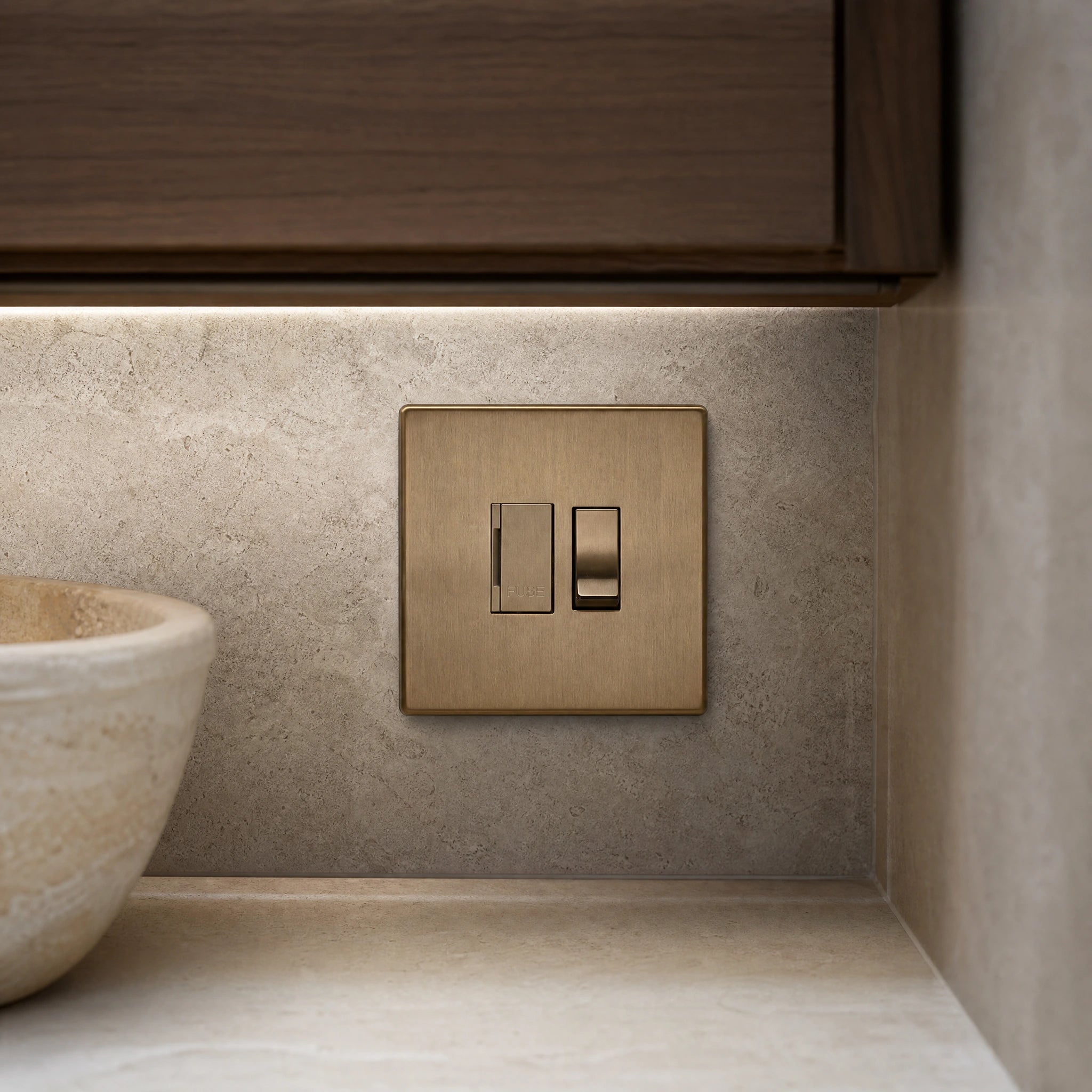 Close-up of a luxury antique brass fused spur installed within discreet below-cabinet utility or kitchen appliance zone in a high-end residence by VORELLI®.