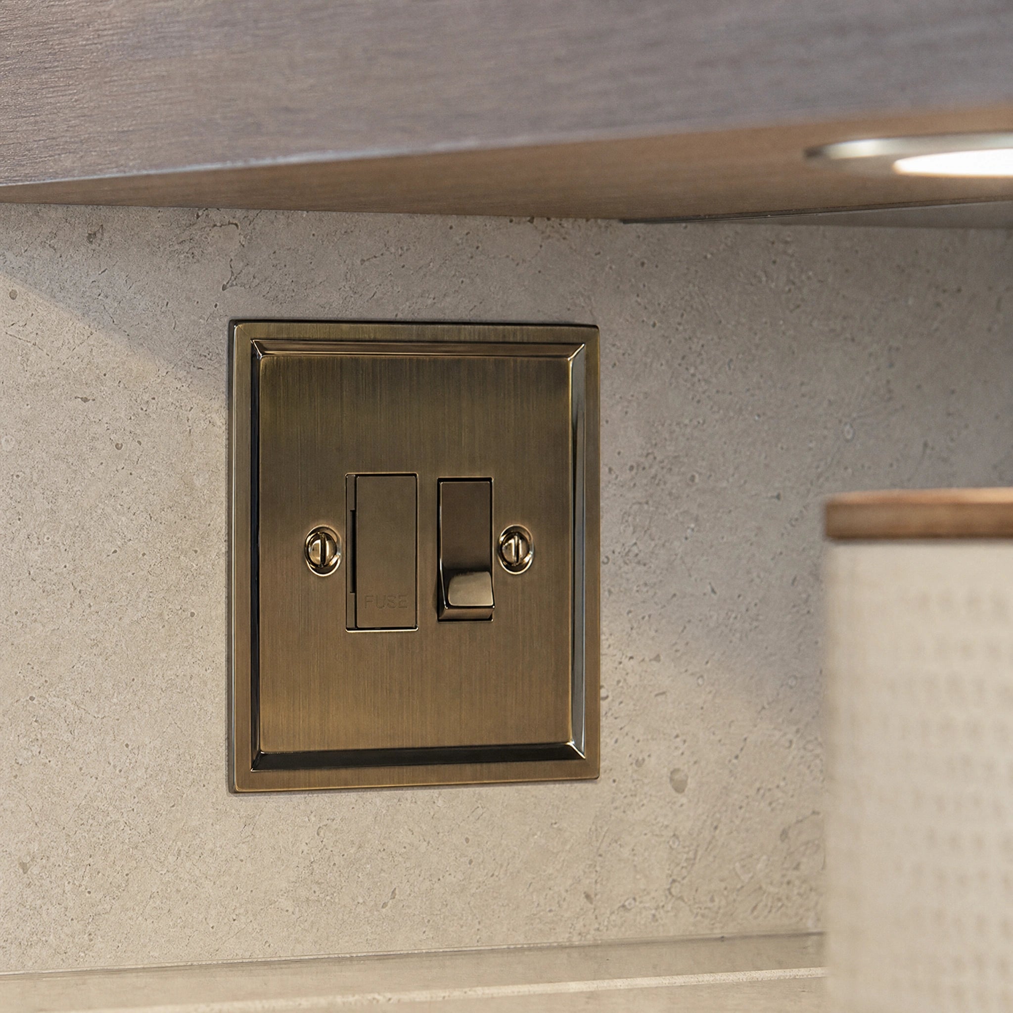Close-up of a luxury antique brass fused spur installed within discreet below-cabinet utility or kitchen appliance zone in a high-end residence by VORELLI®.