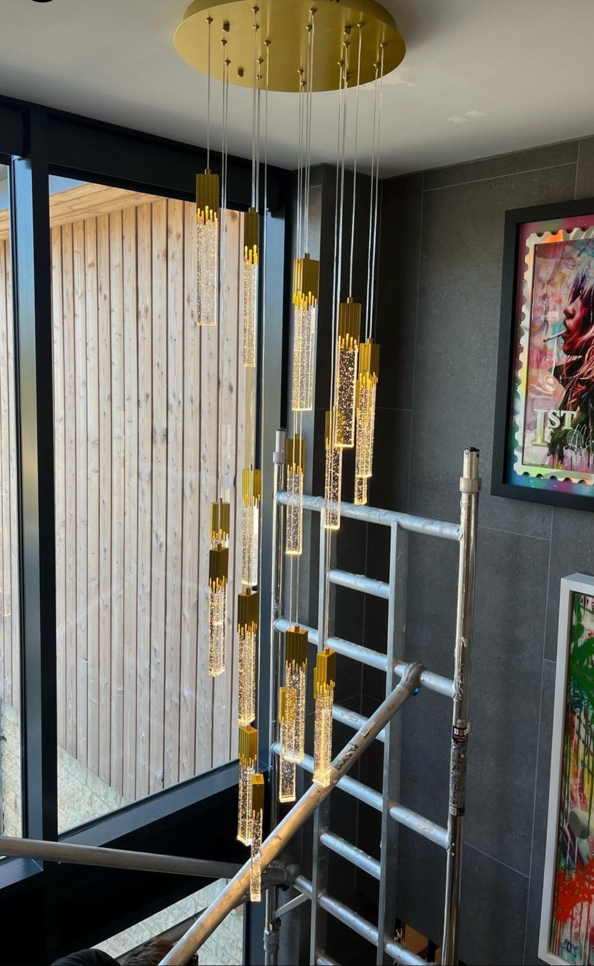 Close view of Halstead crystal pendant staircase chandelier showing suspended glowing glass tubes and gold ceiling plate