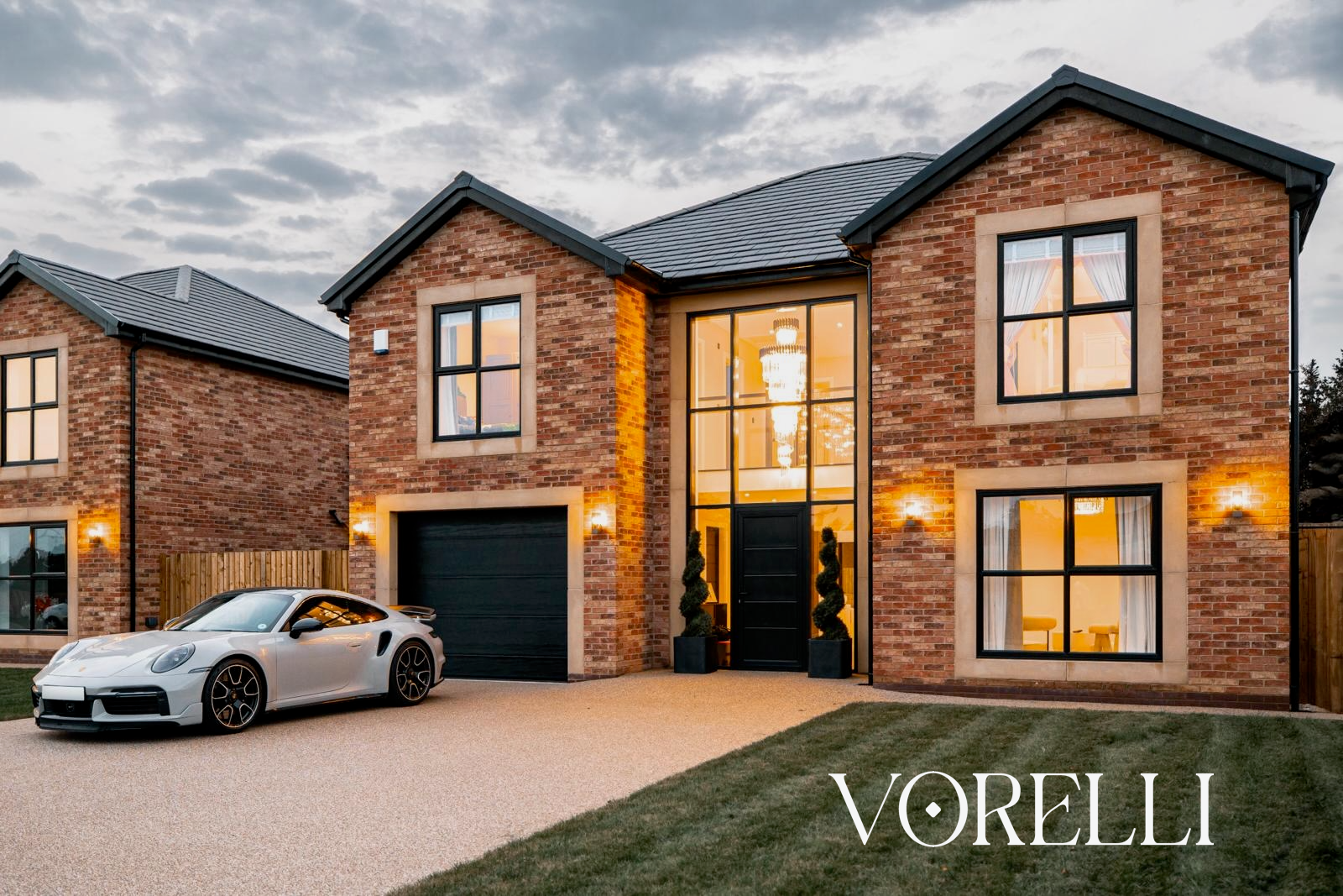 Exterior view of a luxury private residence featuring a bespoke VORELLI® staircase chandelier installation