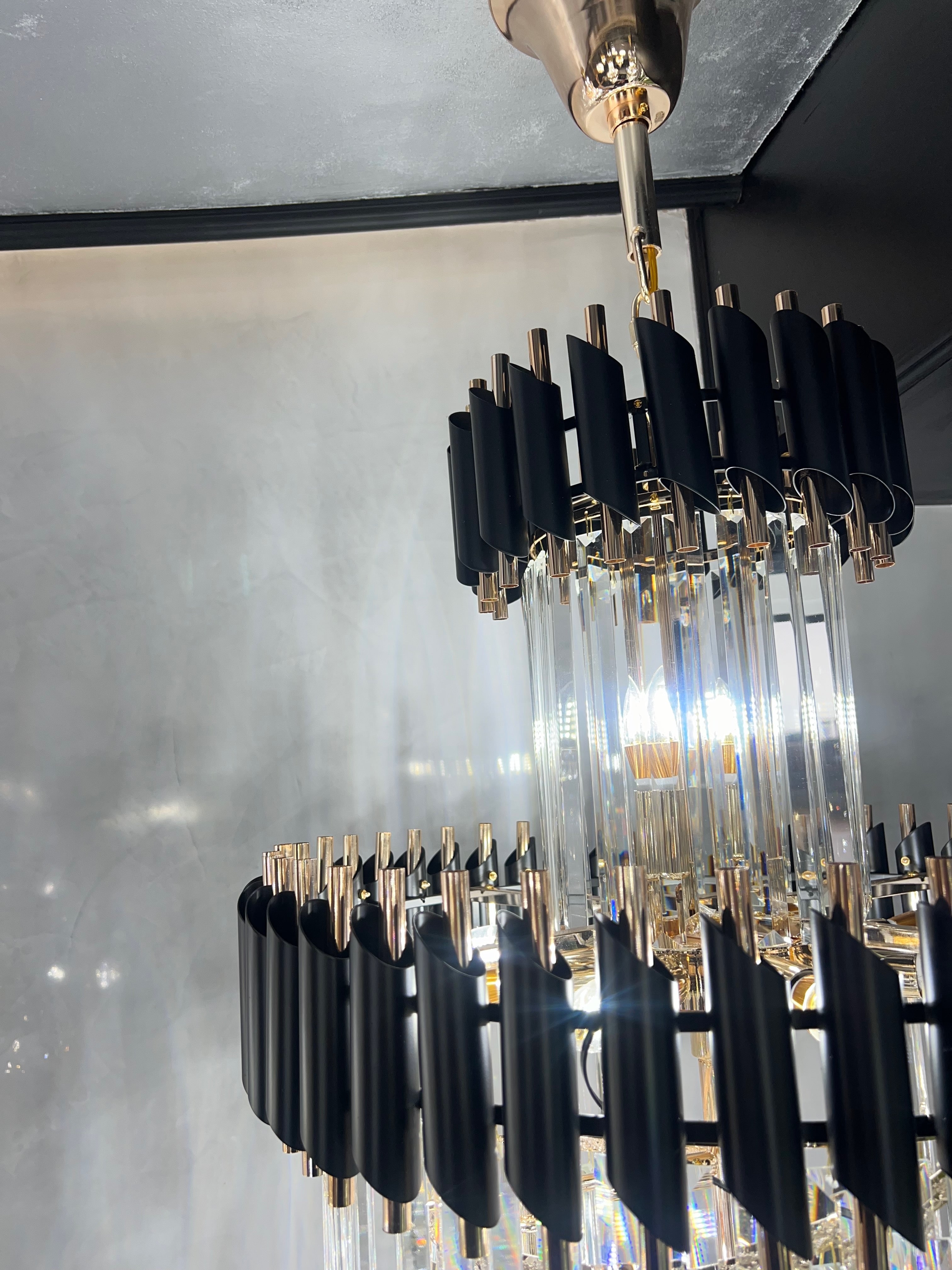 Close-up detail of a modern VORELLI® crystal chandelier featuring black metal fins, gold accents, and vertical glass rods in a luxury interior