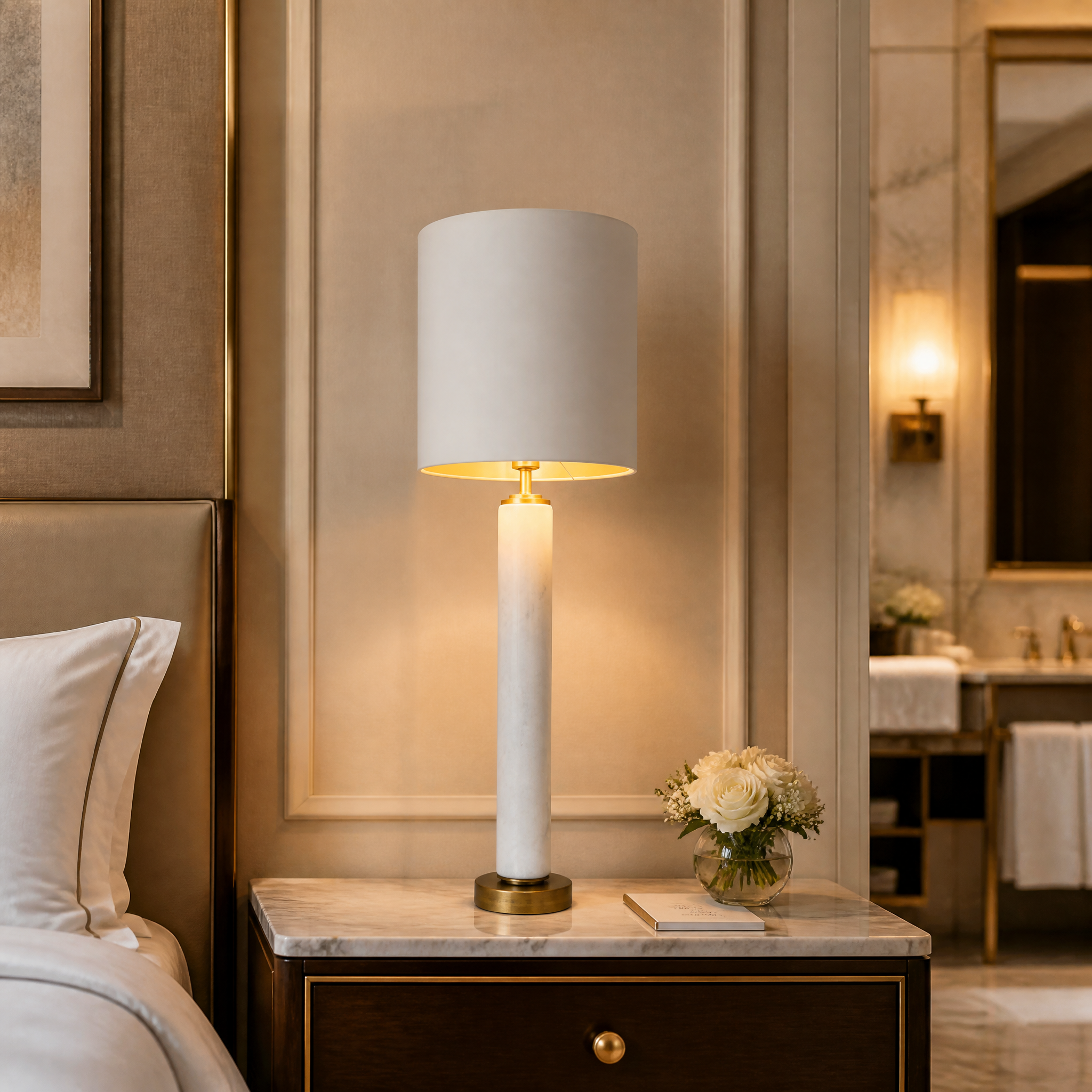 An elegant VORELLI Norvello marble column table lamp casting a warm ambient glow in a sophisticated hospitality lounge or hotel lobby.