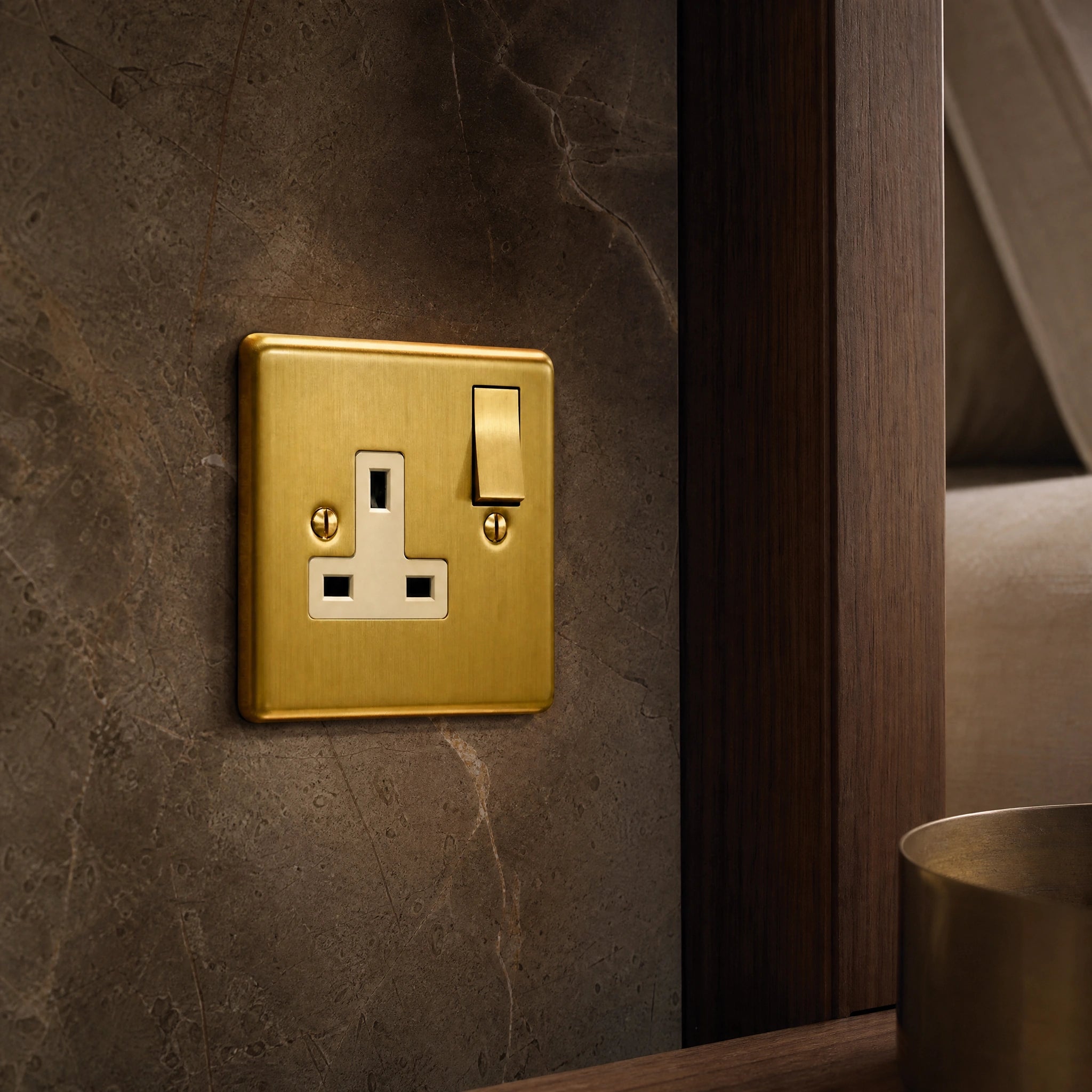 Close-up of a luxury antique brass single socket installed within bespoke bedside joinery or stone wall beside a luxury seating area by VORELLI®.