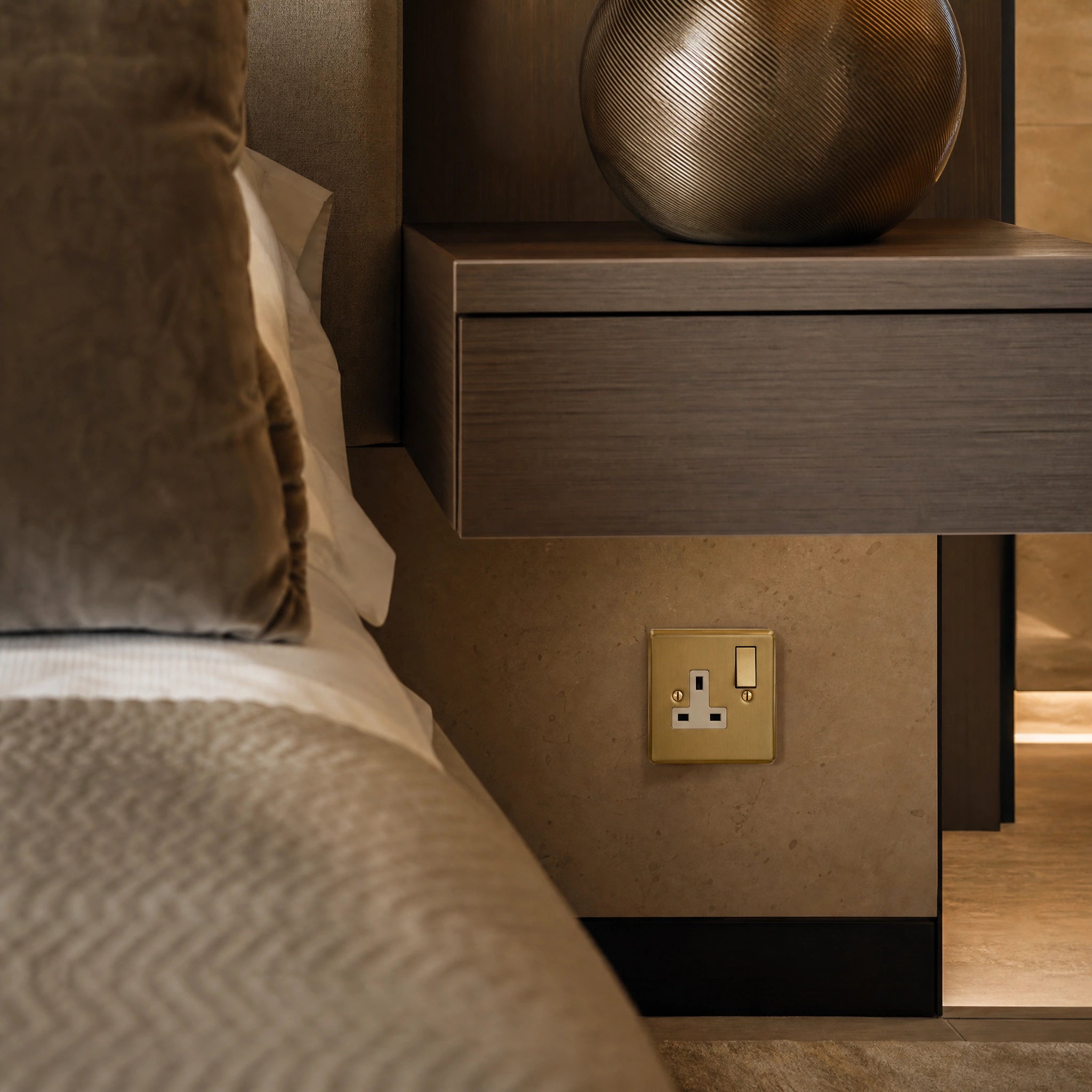 Luxury antique brass single socket installed within bespoke bedside joinery or stone wall beside a luxury seating area in a UHNW interior by VORELLI®.