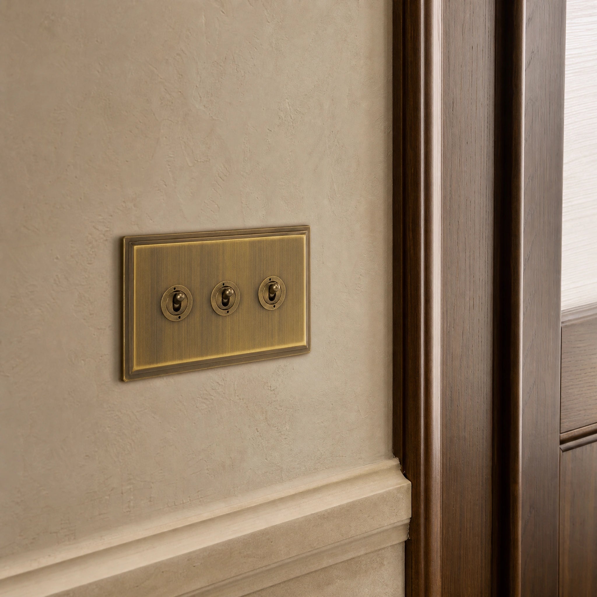 Close-up of a luxury antique brass toggle switch installed within feature wall beside an elegant doorway with refined timber panelling by VORELLI®.