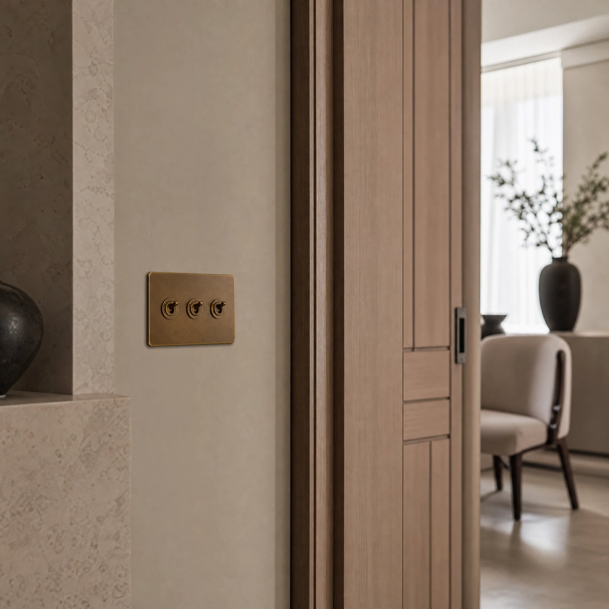 Luxury antique brass toggle switch installed within feature wall beside an elegant doorway with refined timber panelling in a UHNW interior by VORELLI®.