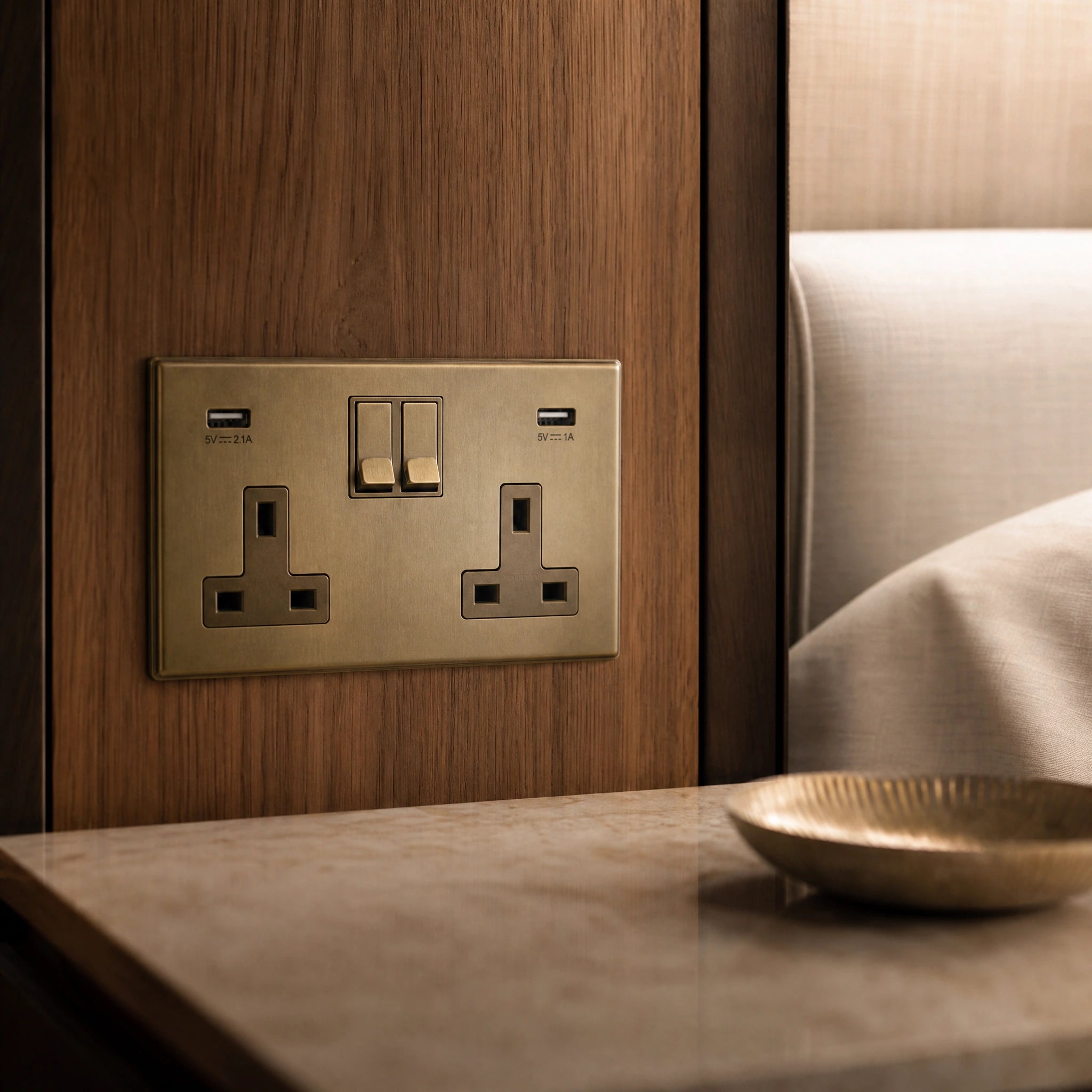 Close-up of a luxury antique brass usb socket installed within bespoke bedside joinery in a luxury bedroom suite by VORELLI®.