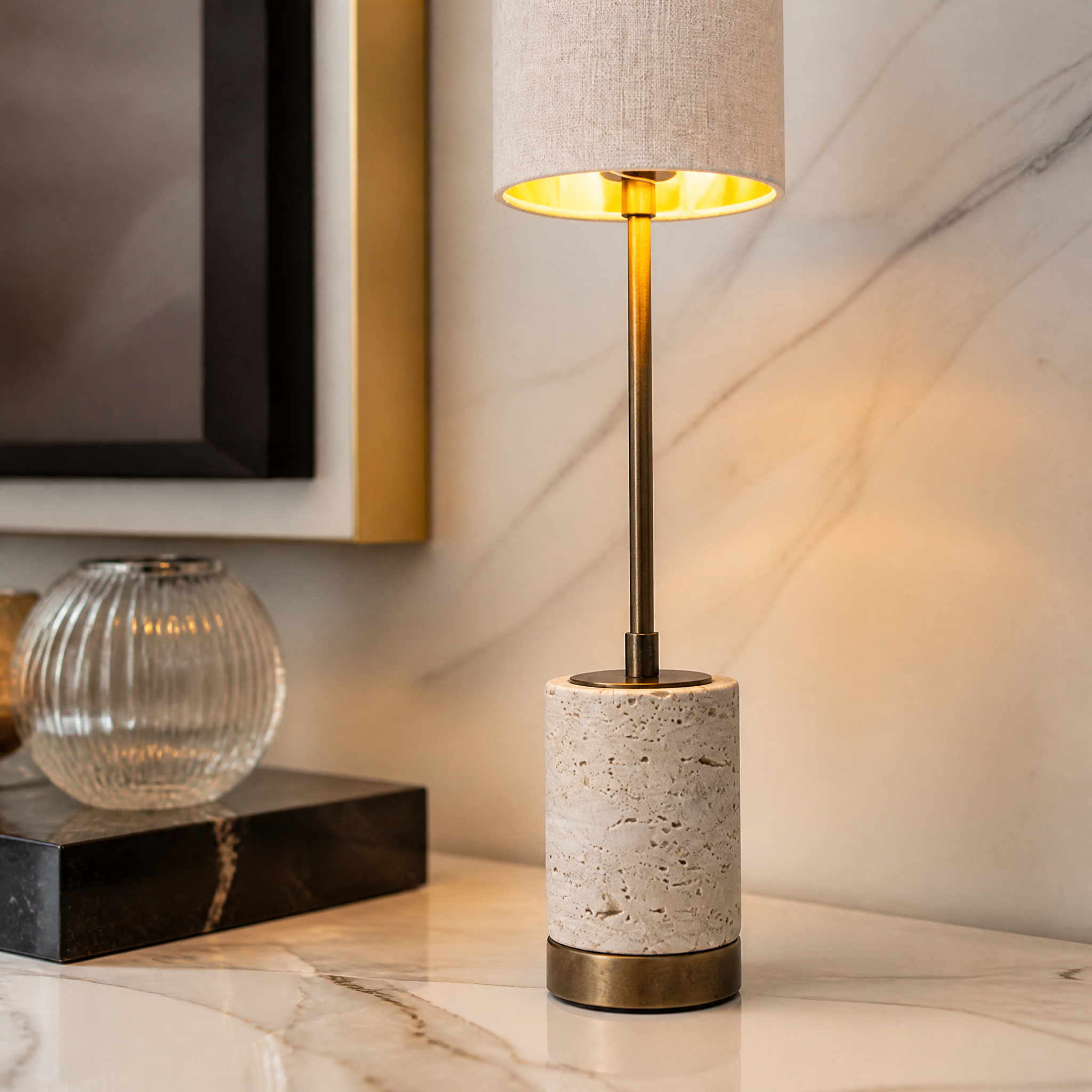 A detailed closeup showcasing the natural textured travertine stone base, refined antique brass stem, and premium linen fabric shade of the VORELLI Valmere H63 table lamp.