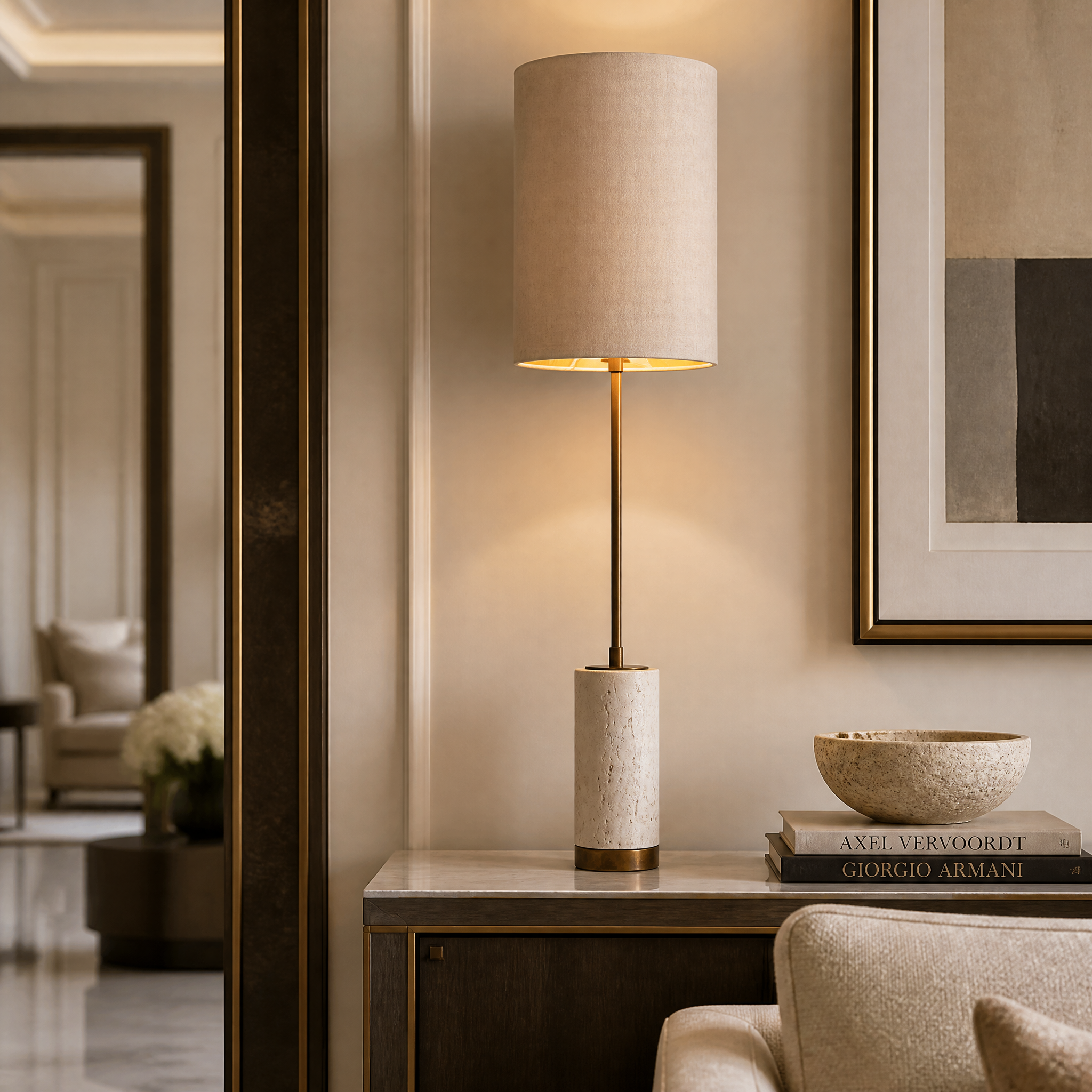 VORELLI Valmere H79 brass table lamp with a natural travertine base and tall linen shade casting warm ambient light on a styled residential console table.